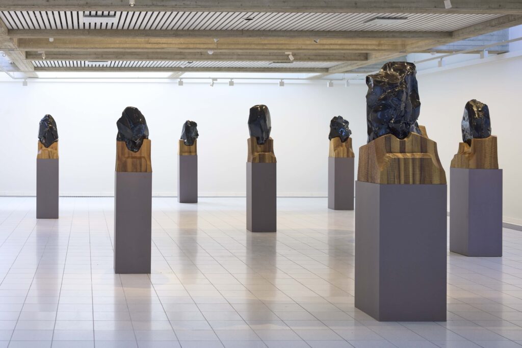 Ryhmä Näkymättömyyskasvot-nimisiä teoksia, 2015, obsidiaani, kastanjapuu.